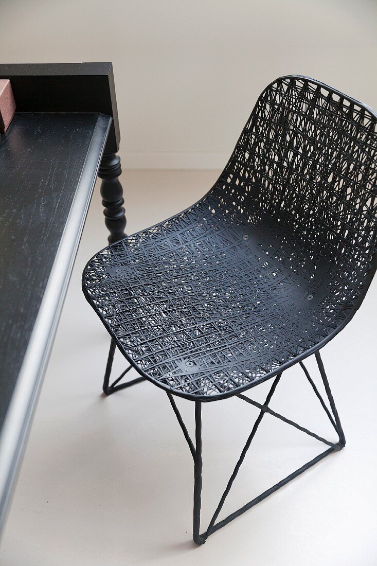 Sitzschale aus schwarzem Geflecht auf Metallgestell vor Tisch