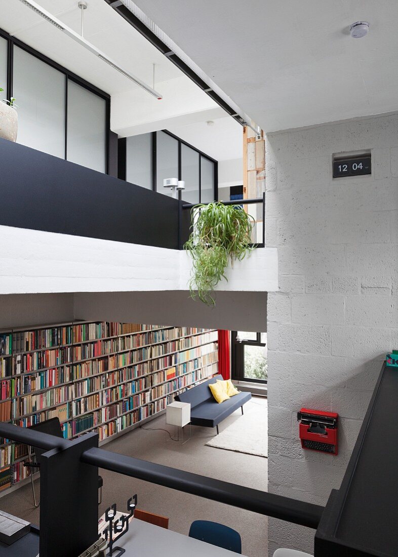 Blick von Galerie in offenen Wohnraum, auf lange Bücherwand und Couch