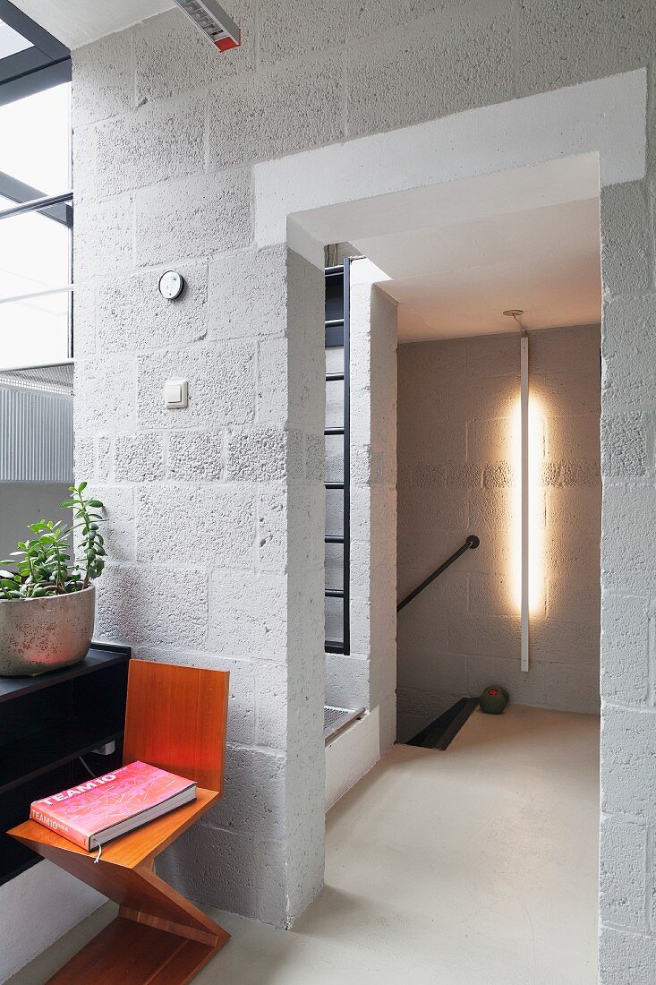 Zig-zag chair against breeze block wall in hallway; vertical strip light on wall in background