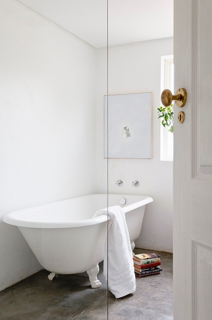 Free-standing, vintage-style bathtub on concrete floor in white bathroom