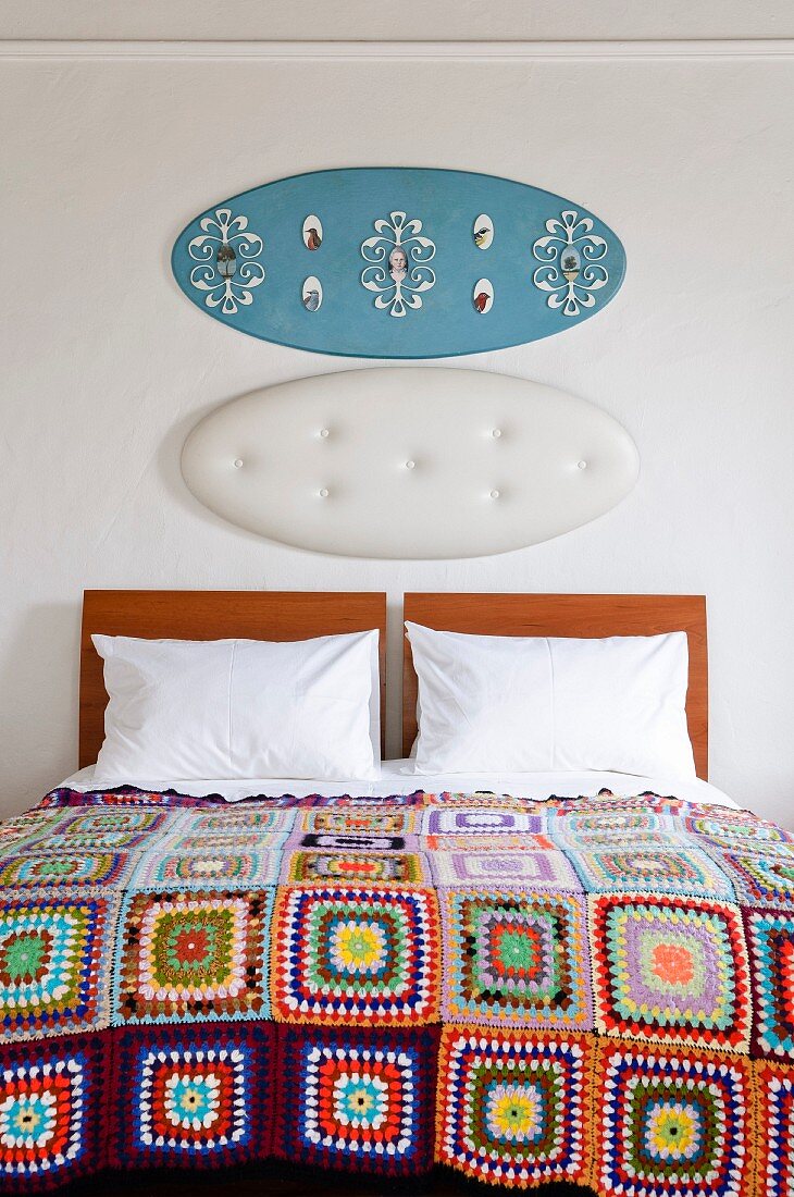 Bed with white pillows, patchwork blanket, and decorated panels above wooden headboard