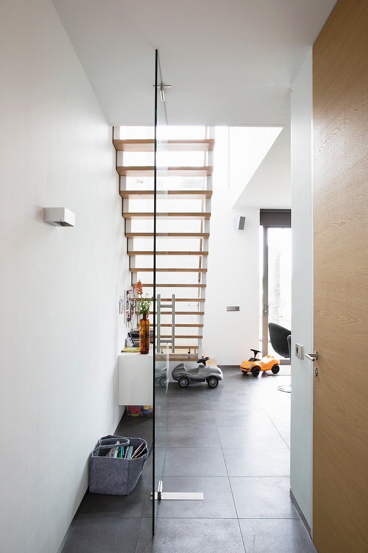 View from hallway into dining area with staircase and ride-on cars on grey tiled floor