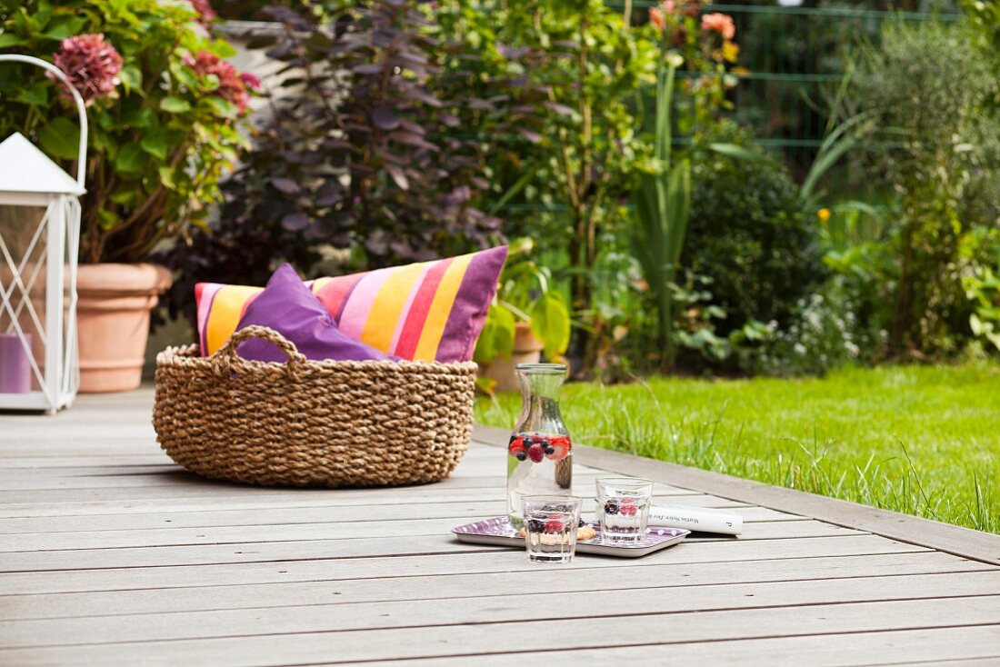 Carafe, glasses and basket of cushions on wooden deck