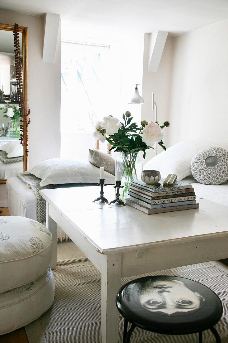 weiße Pfingstrosen auf weiss lackiertem Tisch, in schlichtem Wohnbereich, mit Hocker und Sitzkissenstapel