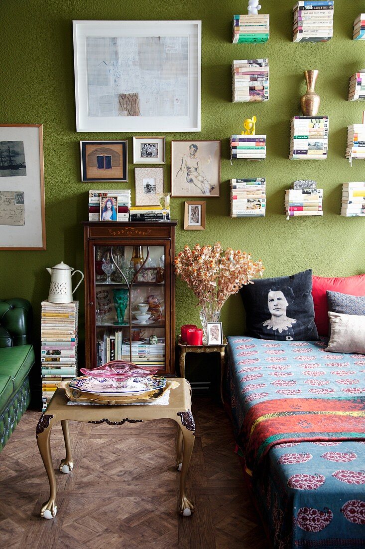 Baroque coffee table next to couch in living room with green wall and stacks of books