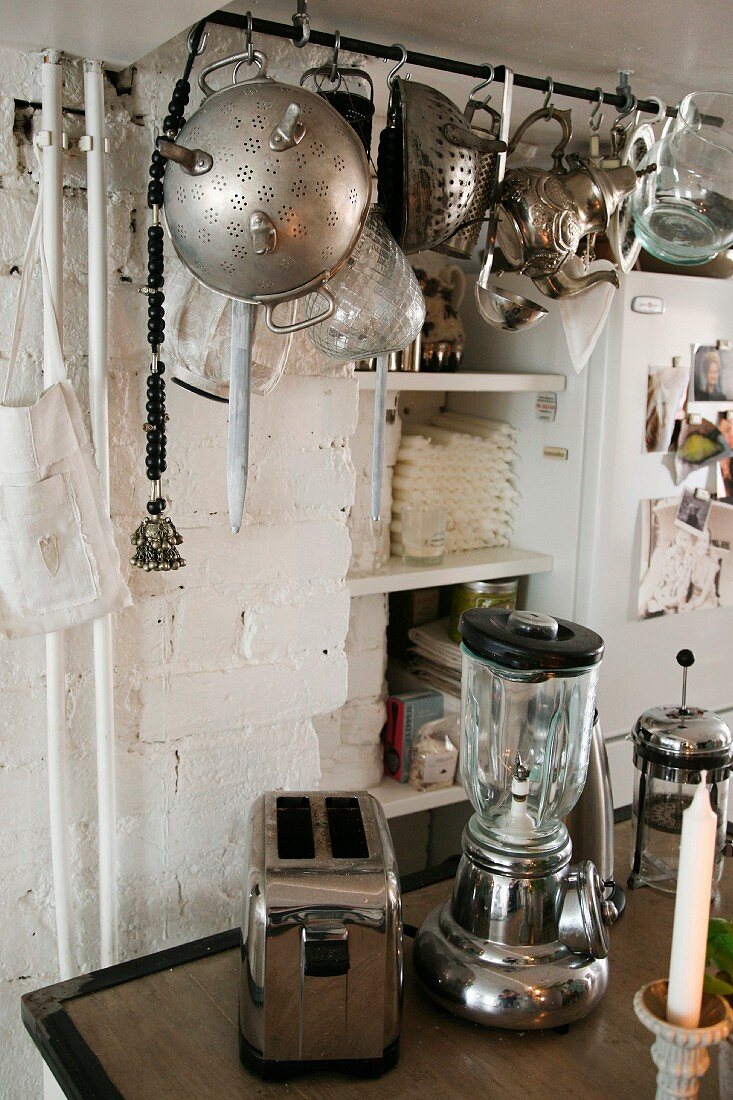 Retro, chrome small kitchen appliances below vintage kitchen utensils hanging from rod