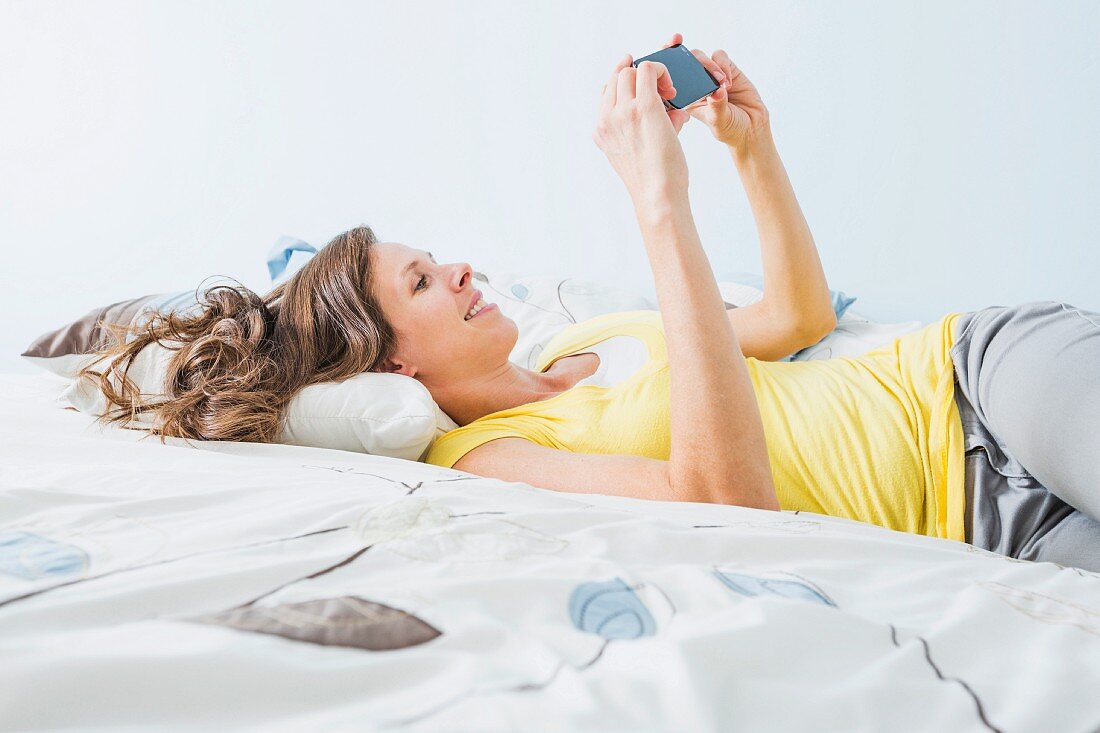 Frau mit Smartphone auf einem Bett liegend