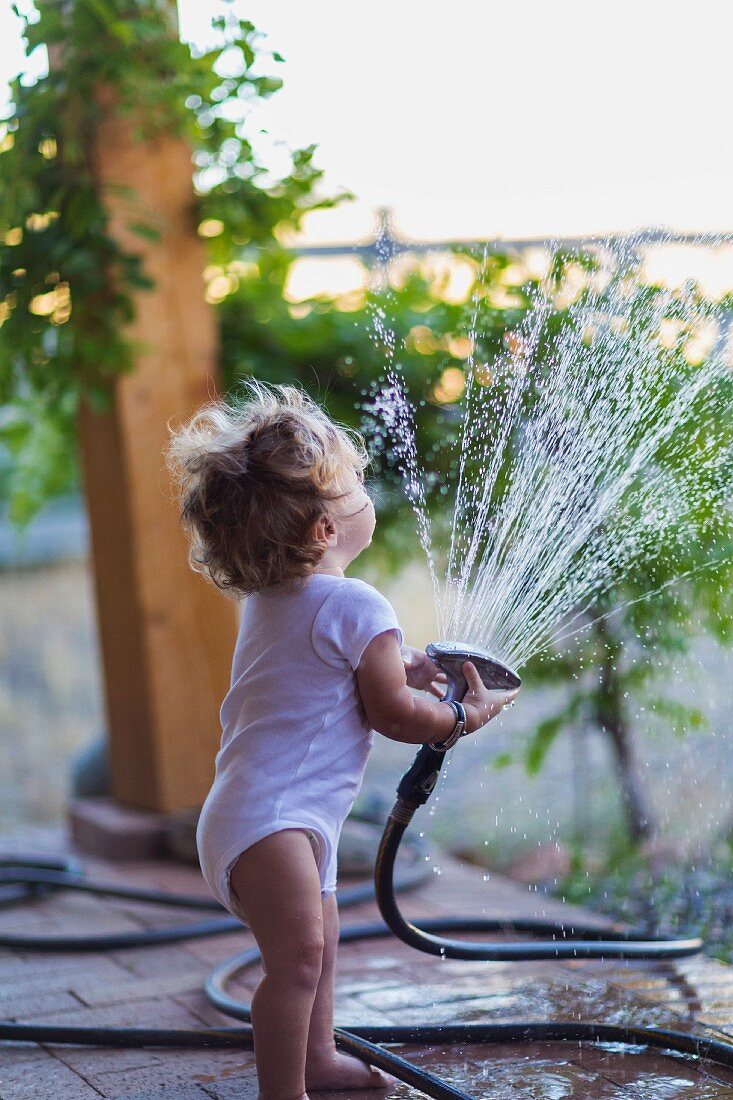 Mit Wasser spielendes Kleinkind auf der Terrasse