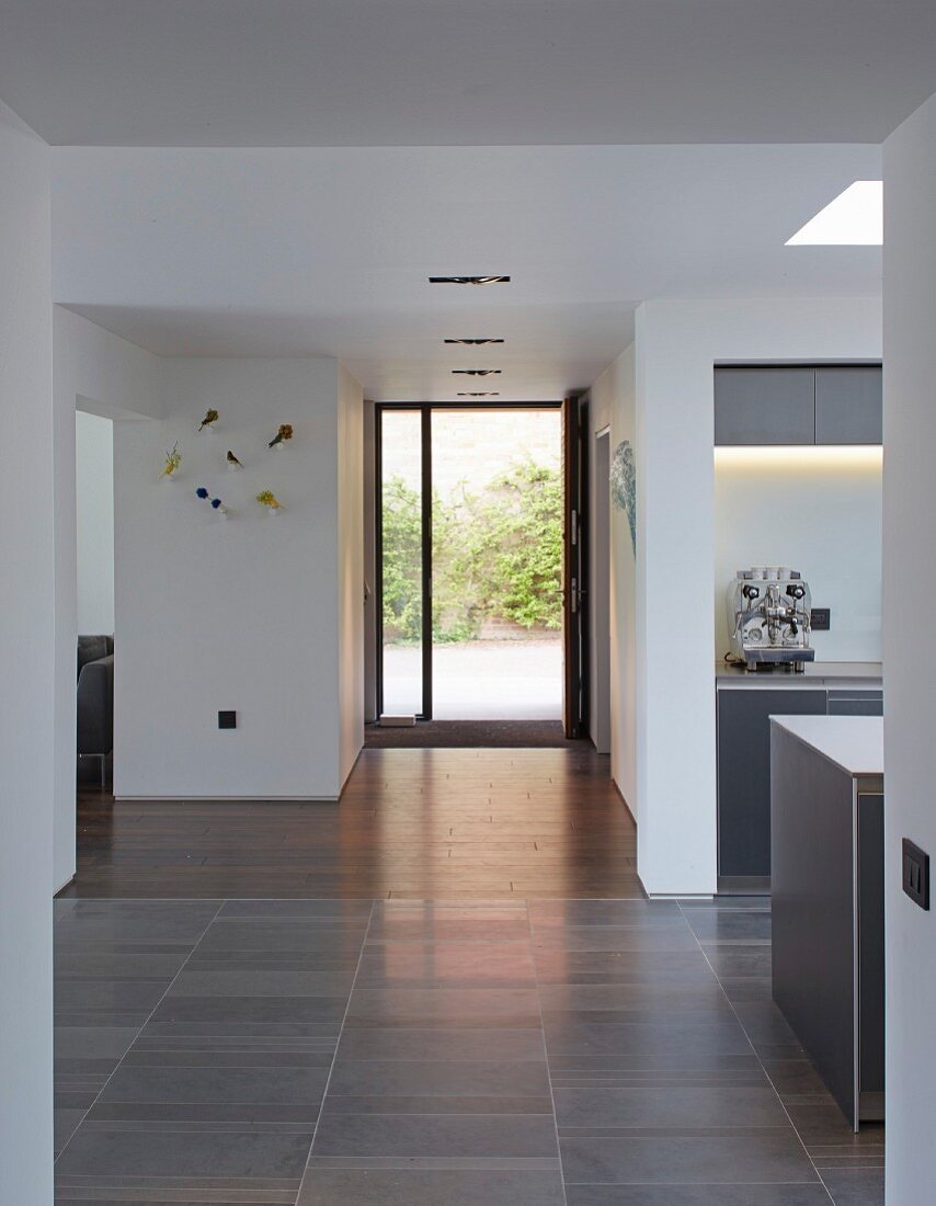 Offener minimalistischer Gangbereich in Weiß, im Hintergrund offene Haustür mit Blick in Innenhof, seitlich teilweise sichtbare Küche in zeitgenössischem Wohnhaus