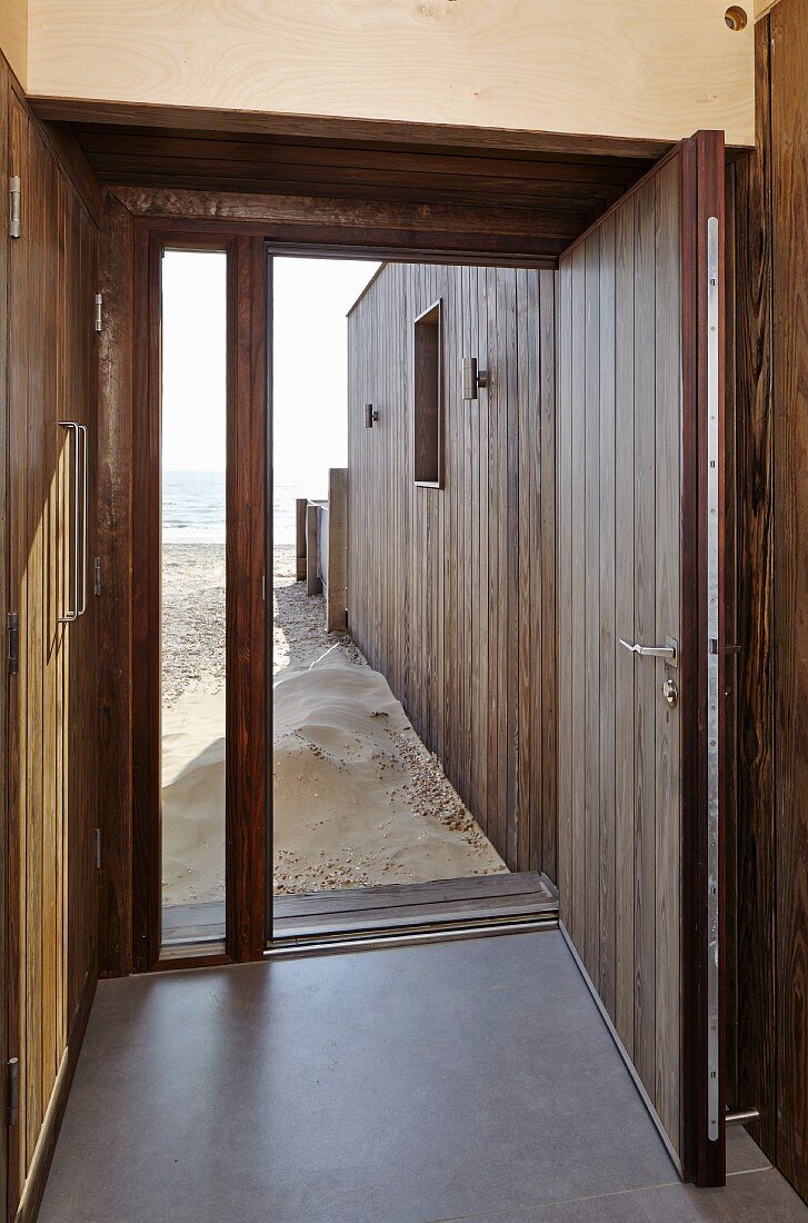 Blick von Hauseingang durch offene Haustür auf Sandstrand und Meer