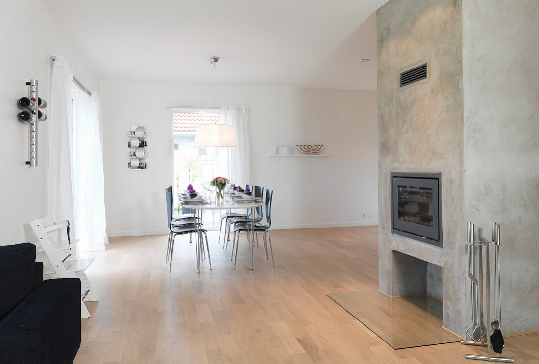 Sparsely furnished interior with exposed concrete chimney breast and festively set table in background