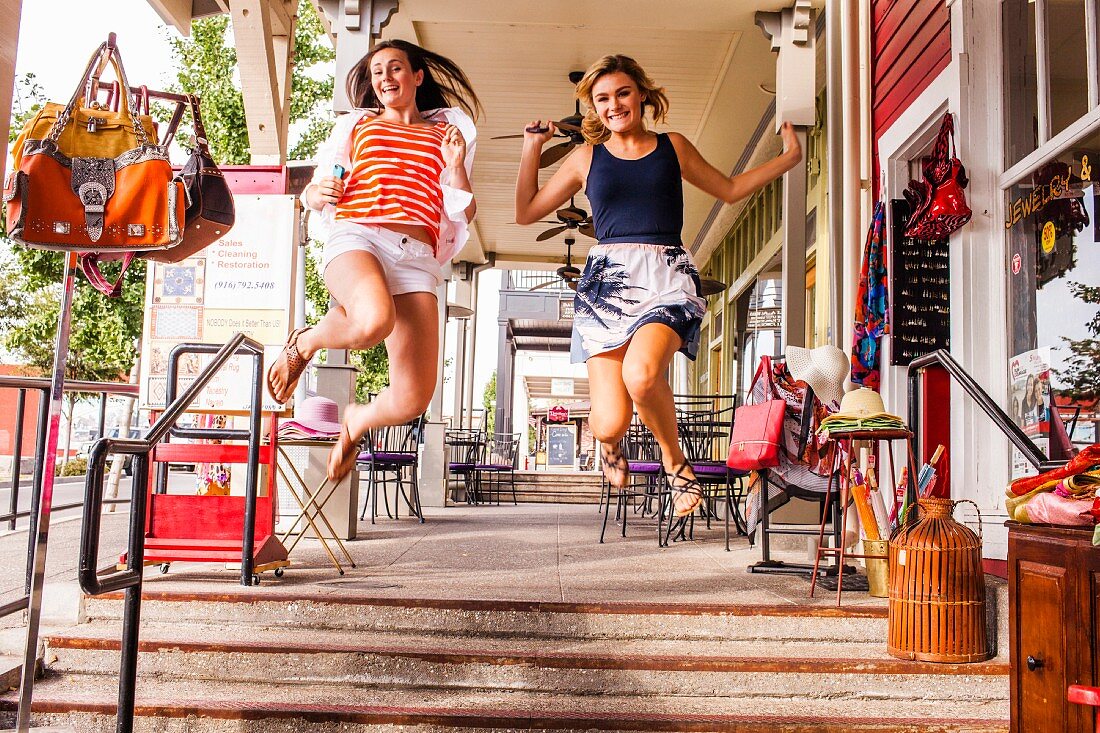 Zwei weibliche Teenager springen vor Freude auf einem Bürgersteig in der Stadt