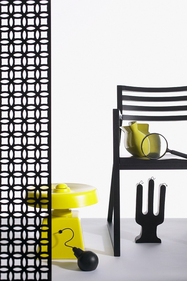 Stuhl und Raumteiler mit grafischem Blütenmuster, arrangiert mit skurrilen Objekten in Schwarz und Gelb