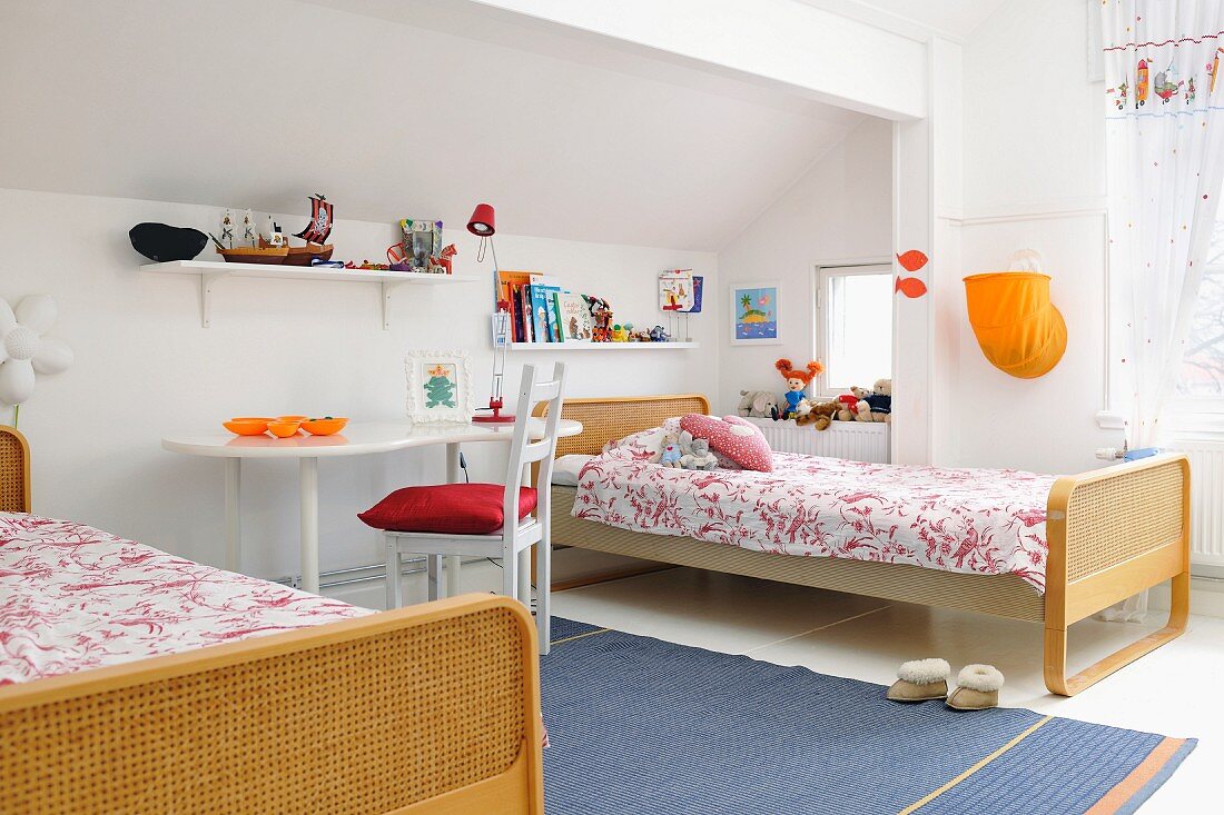 Children's bedroom in converted attic with twin, wicker-framed beds and white table and chair