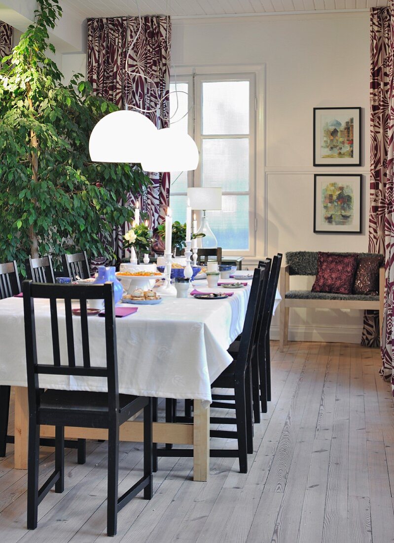 weiße Pendelleuchten über Tisch mit weisser Tischdecke und schwarze Stühle auf rustikalem Dielenboden