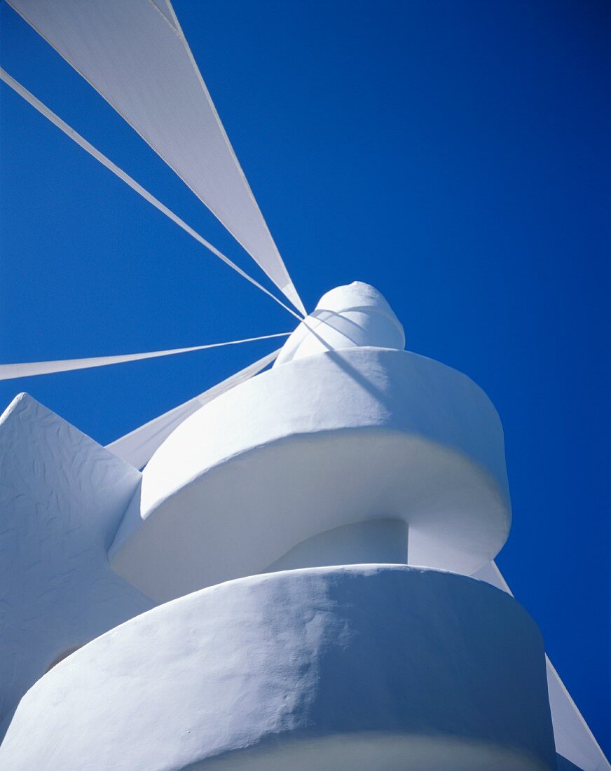 Weisser, gemauerter Treppenaufgang zur Dachterrasse mit Windmühlen-Aufsatz unter blauem Himmel