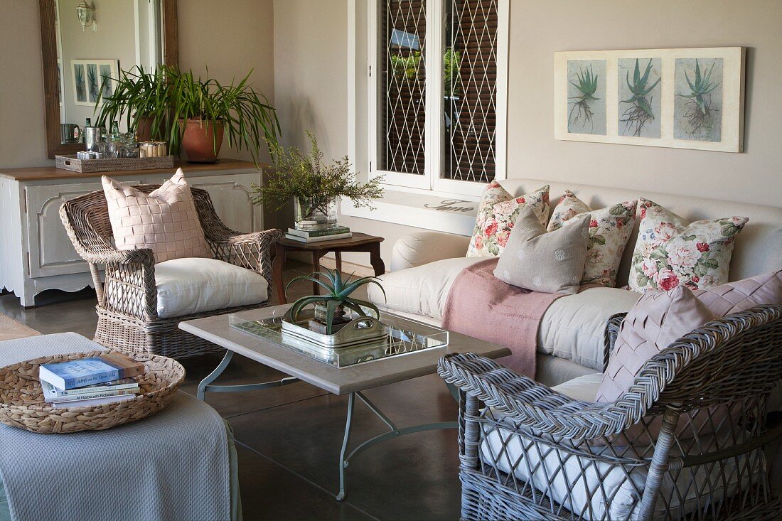 Rattan Sessel und Sofa mit Kissen um Couchtisch auf wohnlich eingerichteter, geschützter beigefarbener Veranda