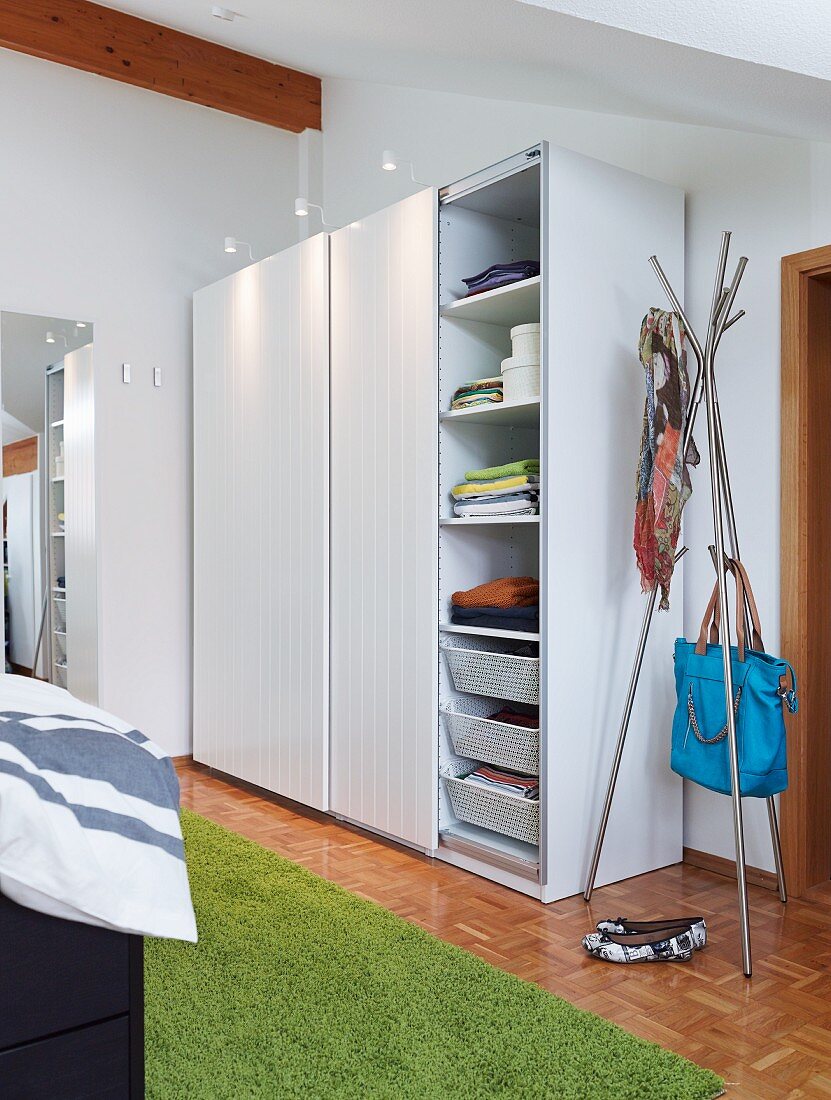 A storage solution on a bedroom consisting of a simple cupboard with sliding doors and spotlights next to a hat stand