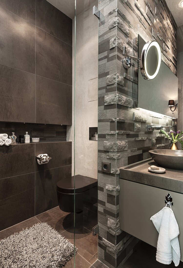 WC neben dunkler Fliesenwand mit Ablagenische und Glasabtrennung; Kalksteinrelief als Waschtisch-Rückwand