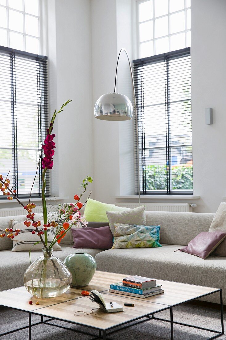 Couchtisch und beigefarbenes Designer Sofa, Bogenlampe in hohem Wohnzimmer mit hohen Sprossenfenstern