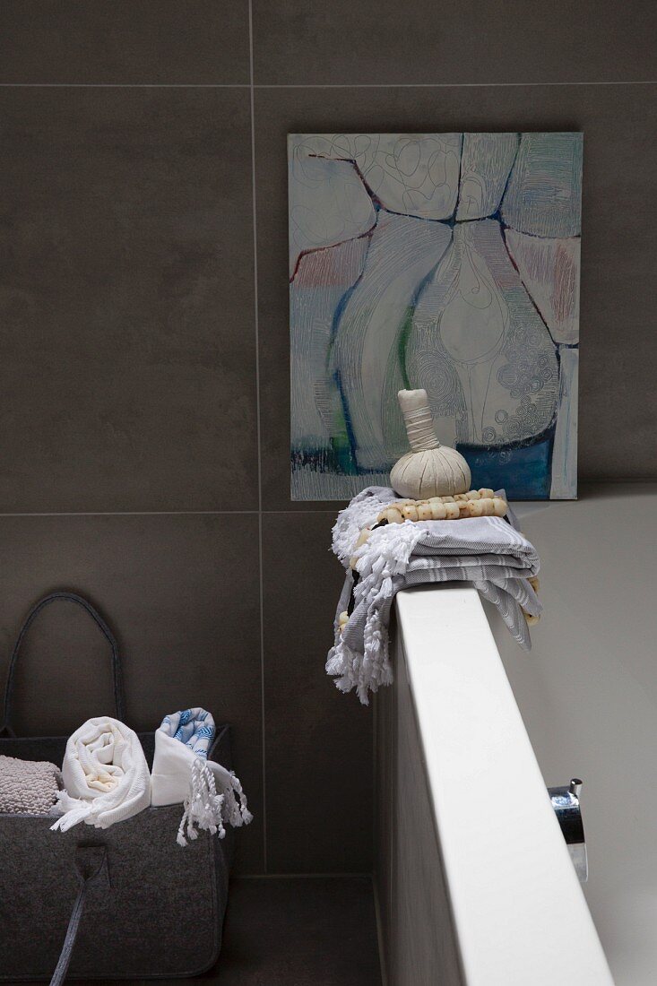 Handtücher auf Badewannenrand vor modernem Bild an gefliester Wand