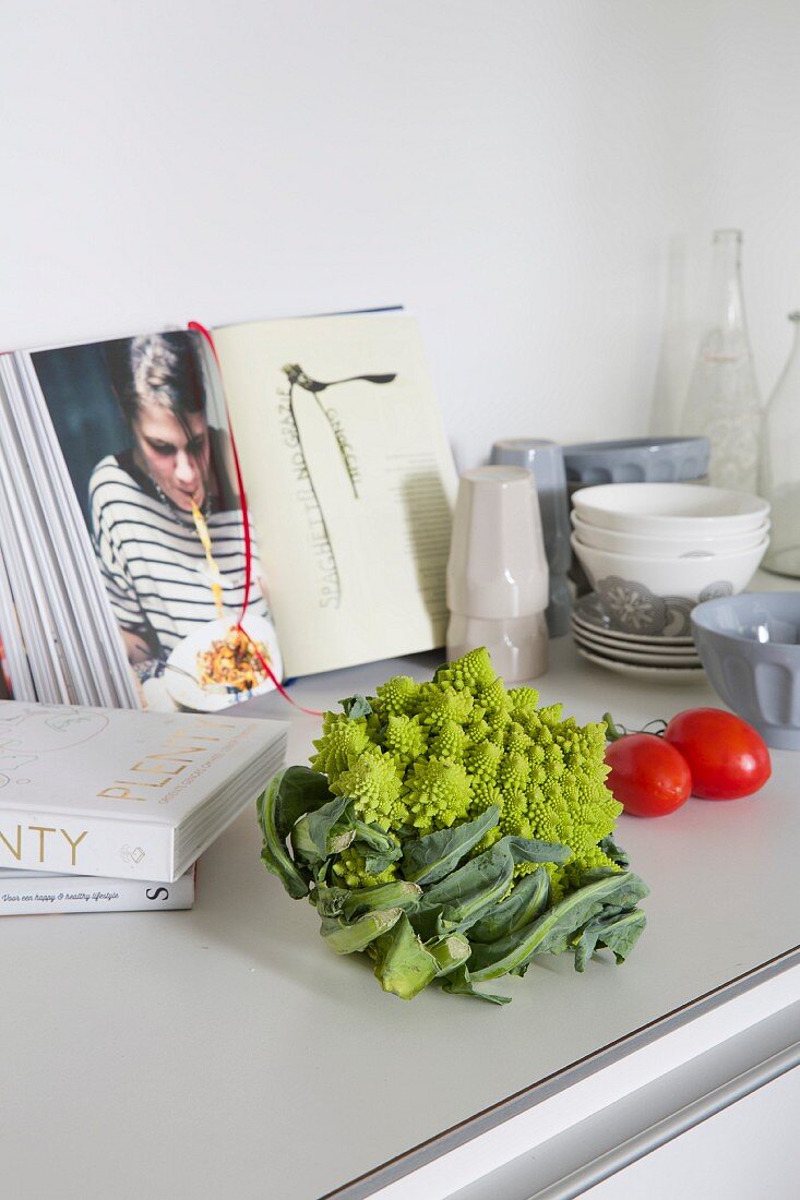 Romanesco und Tomaten vor aufgeschlagenem Kochbuch auf Küchenzeile