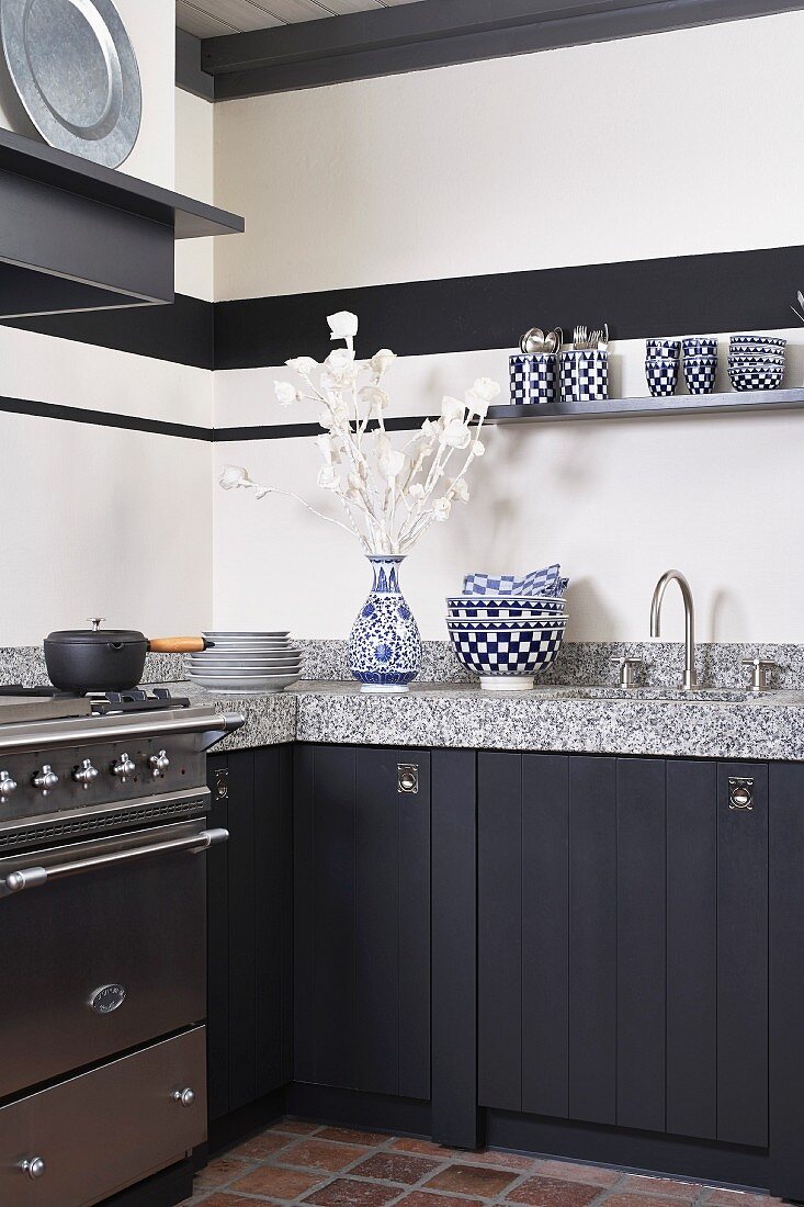 Unterschränke in Einbauküche mit dunklen Fronten, Edelstahlherd und Arbeitsplatte aus Granit; weissblau karierte Schalen