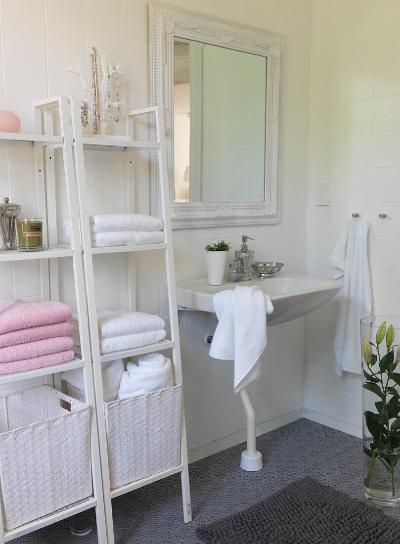 weiße Regale mit Handtüchern und Wäschekorb neben Waschbecken in Bad mit romantischem Charme