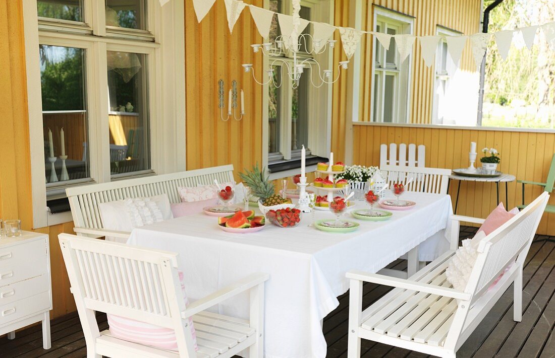 weiße Holzmöbel um festlich gedeckten Tisch auf Veranda eines gelben Holzhauses