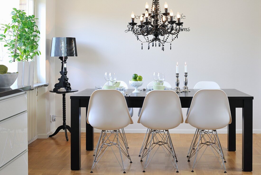 Classic chairs with white shell seats on metal frames around black dining table below chandelier in modern dining room