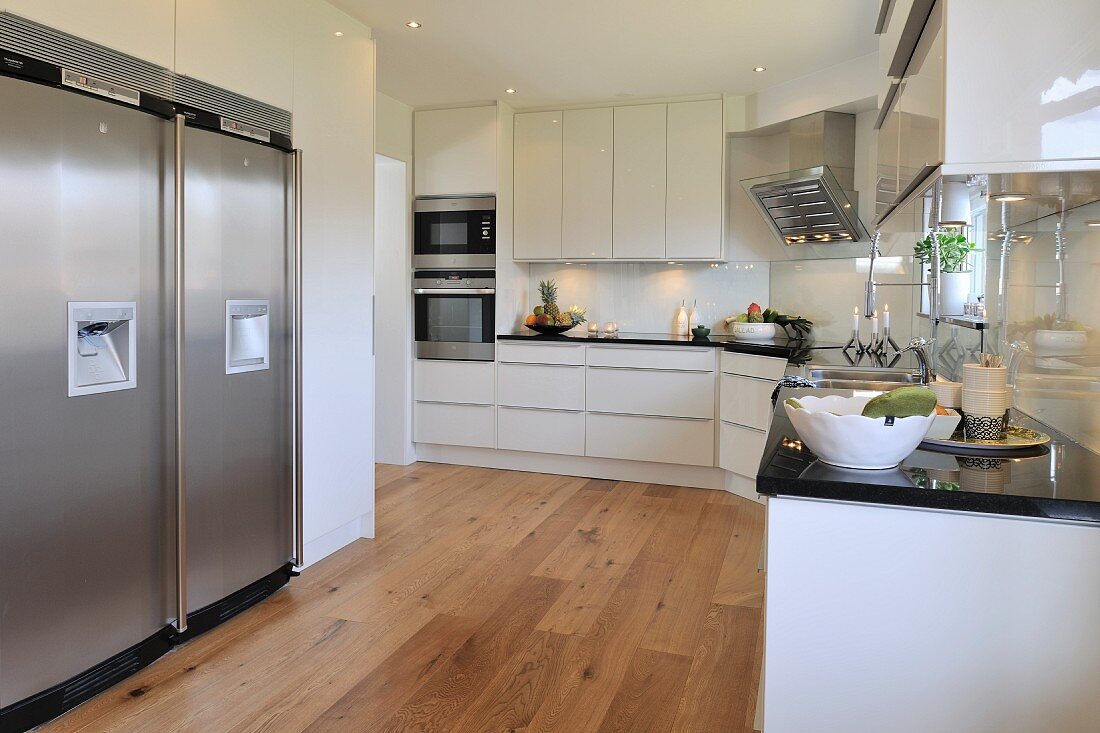 weiße Designerküche mit Dielenboden, seitlich Edelstahl Kühlschrankkombination in Nische