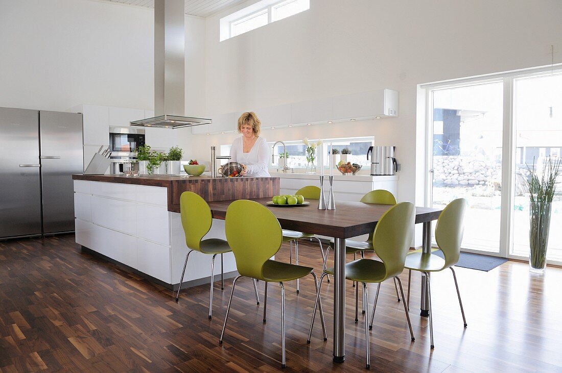 Esstisch mit grünen Retro Stühlen, anschliessend die Küchentheke, in eleganter, offener Küche mit Walnussparkett