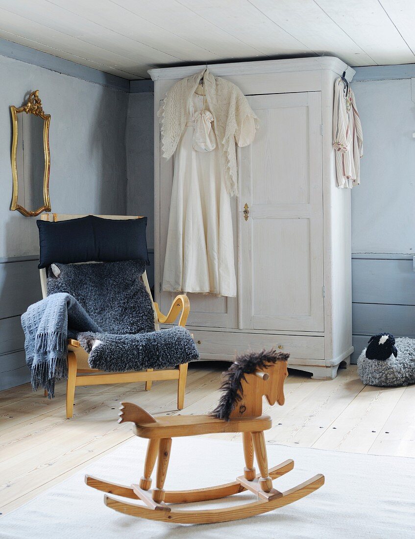Rocking horse, armchair with grey sheepskin blanket and white farmhouse cupboard in corner of rustic room