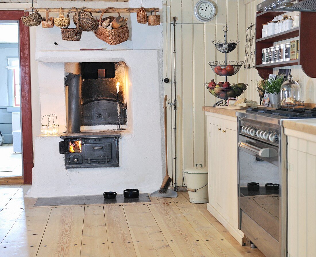 Rustikale Küche mit schlichtem Dielenboden, über eingemauertem Kaminofen Körbe auf Stange gehängt