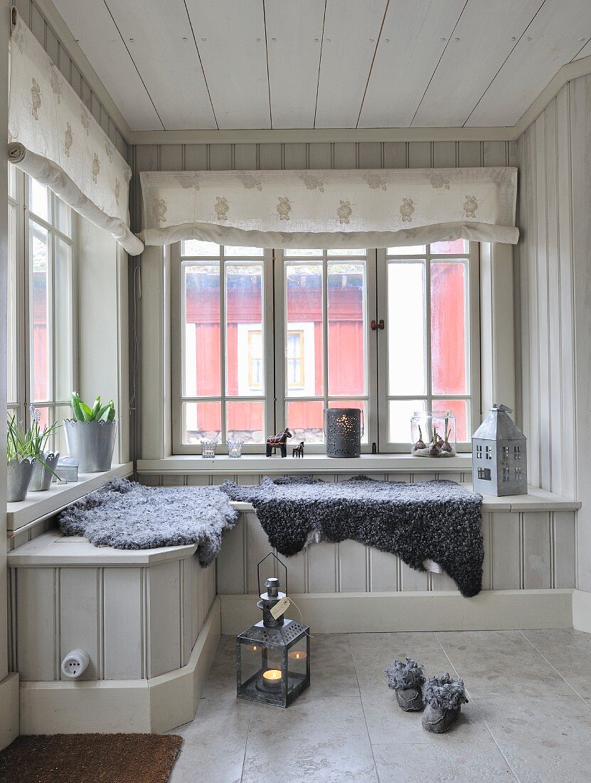 Grey sheepskin blankets on window seat in wood-clad conservatory with fabric roller blinds on lattice windows