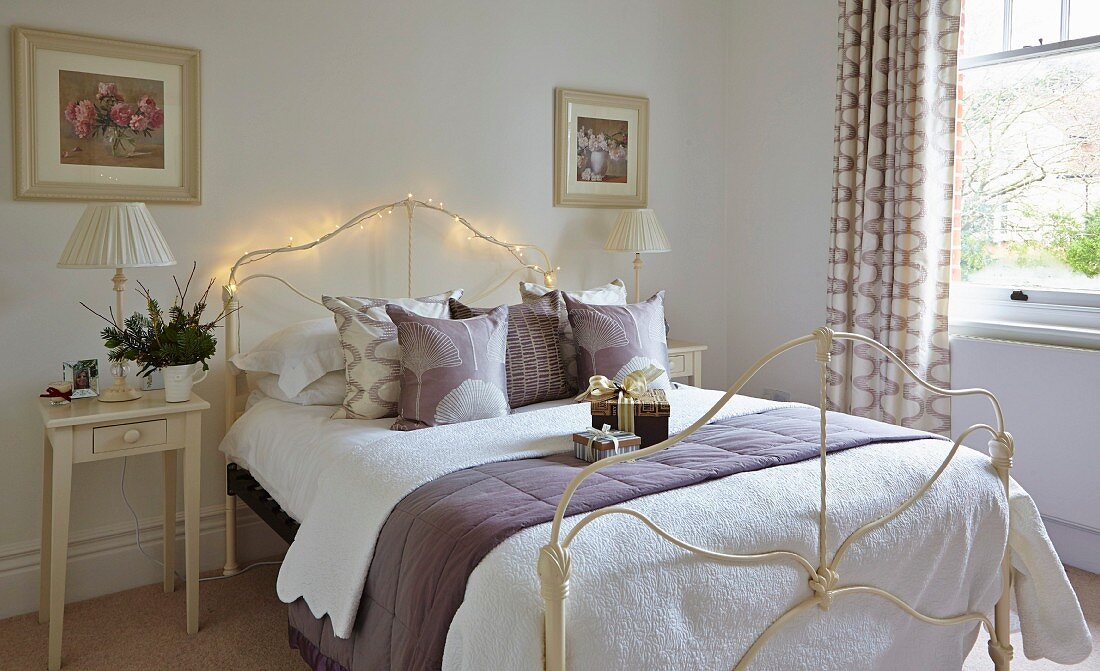 Schmiedeeisernes Bett mit Lichterkette dekoriert in schlichtem Schlafzimmer
