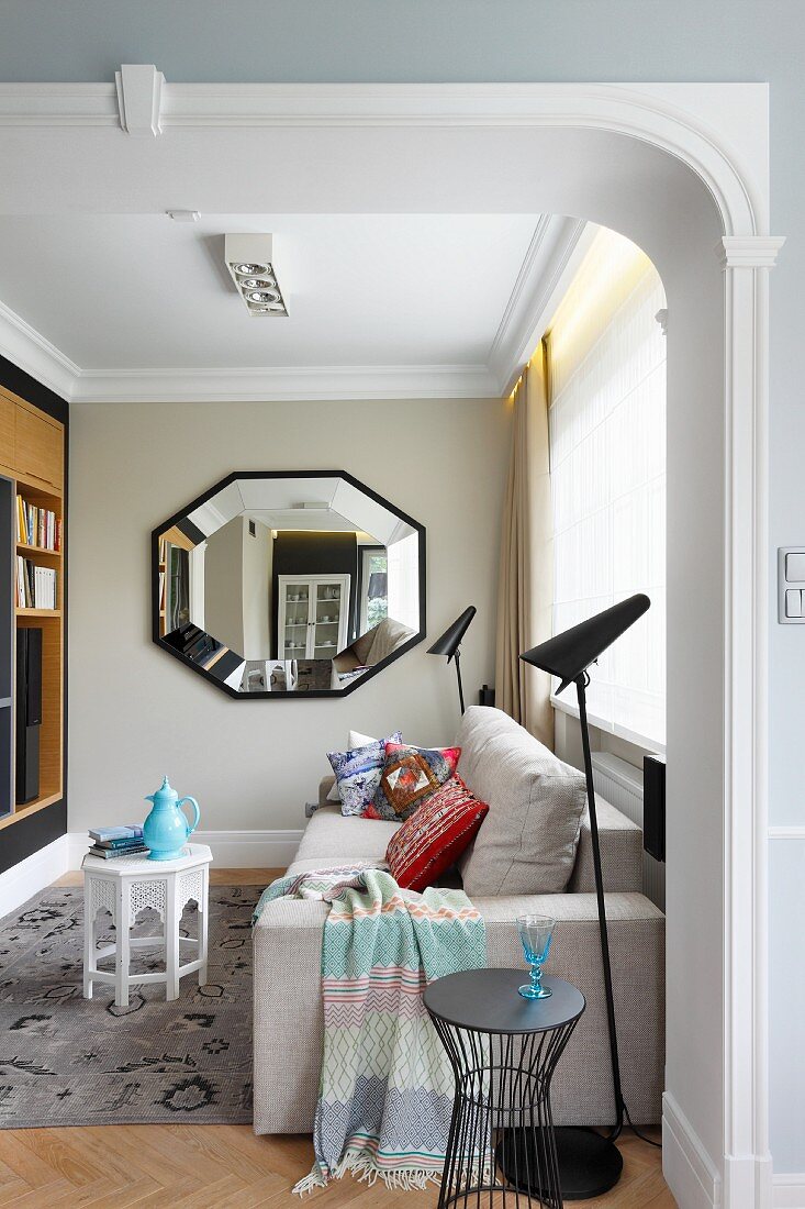 View through wide, open doorway of modern pale couch, black standard lamp and octagonal mirror