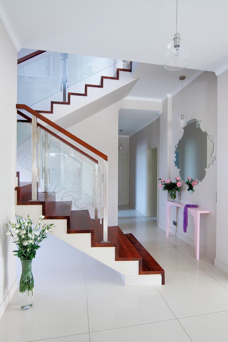 Elegant white hallway with glossy floor tiles and staircase with exotic-wood treads and risers