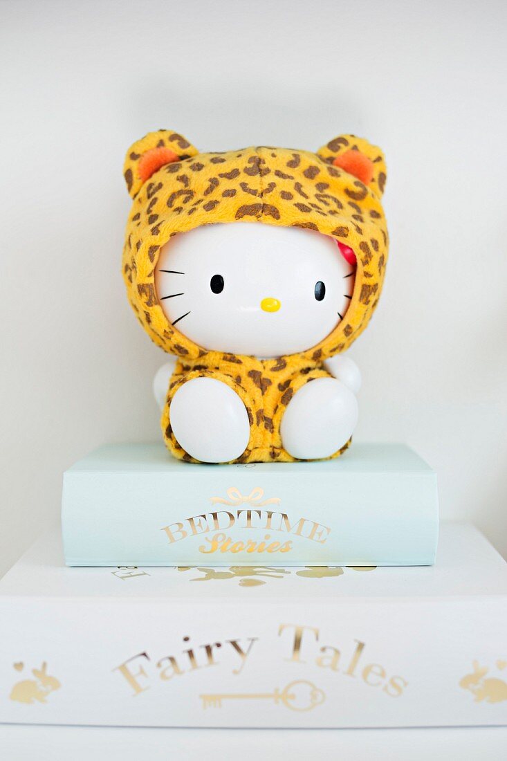 Hello Kitty figurine wearing leopard-print onesie sitting on books with gilt lettering on spines