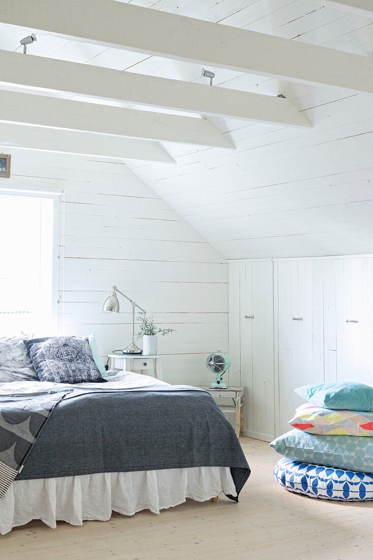 Doppelbett und Kissenstapel vor Einbauschrank in holzverkleidetem Dachzimmer