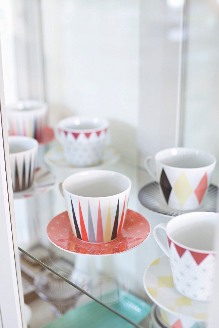 Collectors' cups and saucers with retro, graphical patterns on glass shelves in display case
