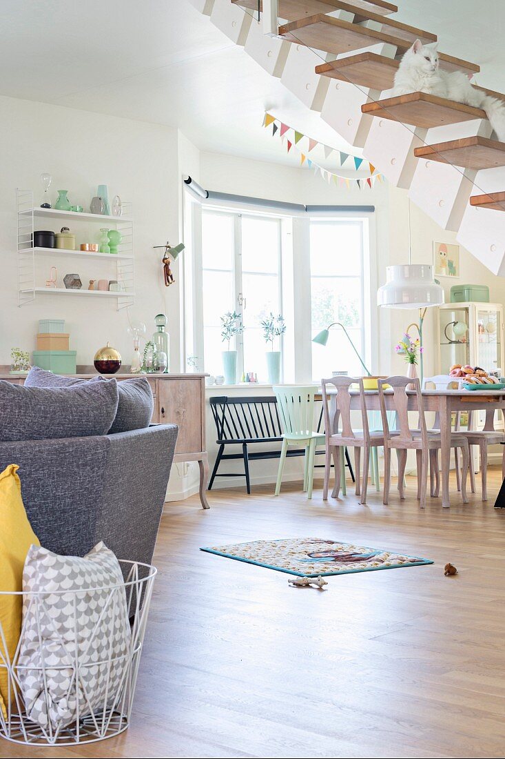 Sofa und Essplatz im offenen, pastellfarben dekorierten Wohnraum und Katze auf freitragender Treppe