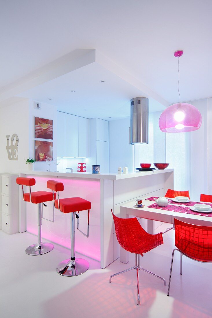 Schalenstühle und Barhocker in leuchtendem Rot an weißem Esstisch und Küchentheke