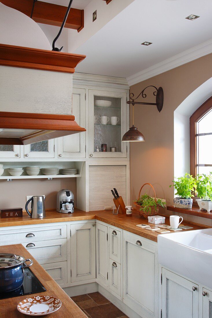 Kitchen counter with wooden worksurface and white, country-house-style base and wall units