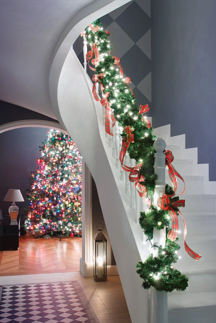 Mit Tannenzweigen verziertes Treppengeländer, seitlich Blick durch Rundbogen auf geschmückten Weihnachtsbaum