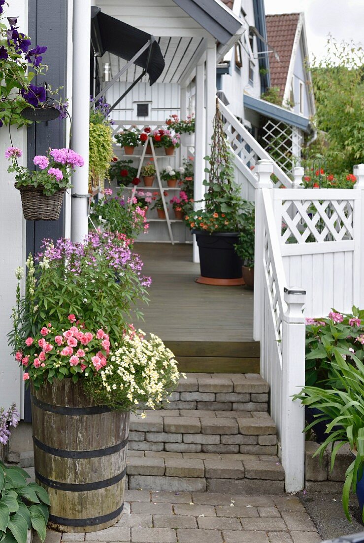 Blühende Blumen im Pflanzentrog vor Treppe zur Veranda, mit weißem Holzgeländer