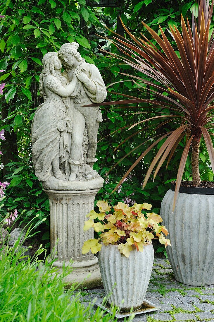 Potted plants around romantic statue of couple on plinth in garden