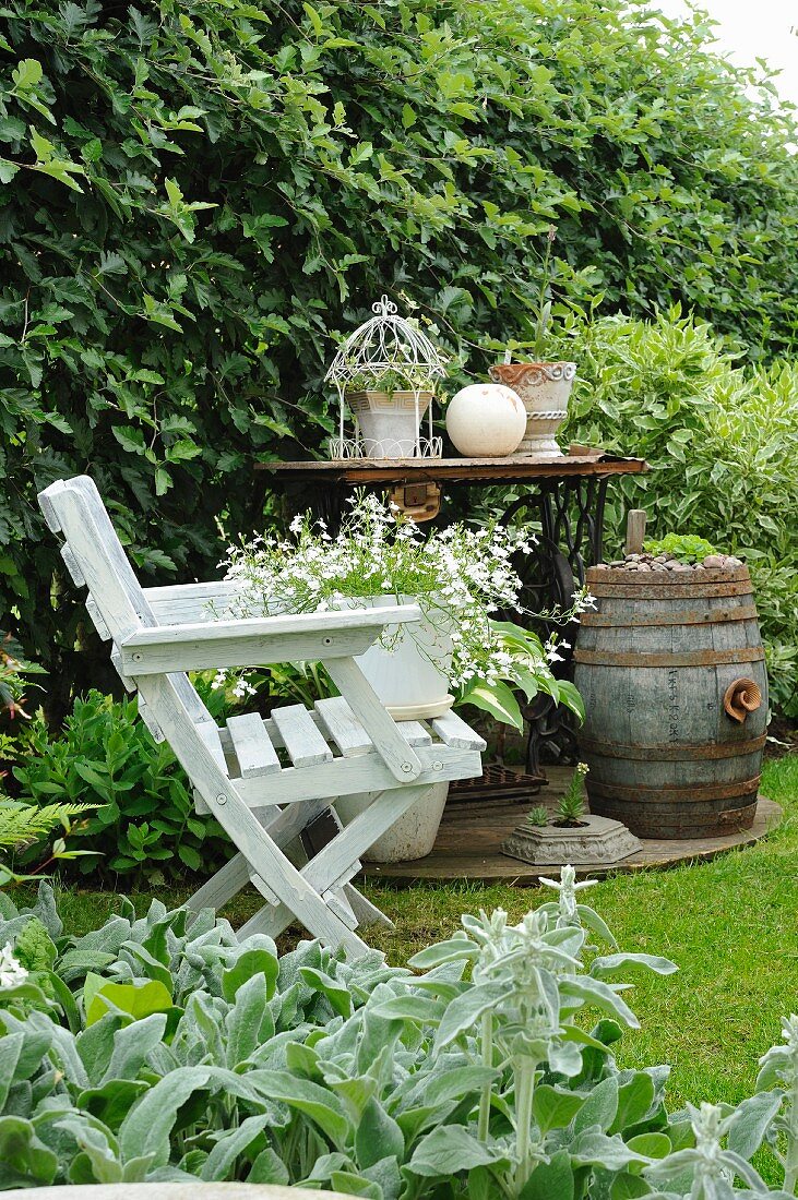 Blumetopf auf weißem Holzstuhl vor Vintage Nähmaschine als Gartentisch und Fass