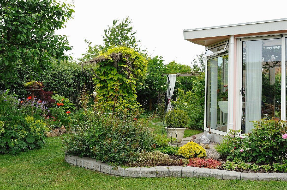 Summery garden with herbaceous border in front of conservatory extension