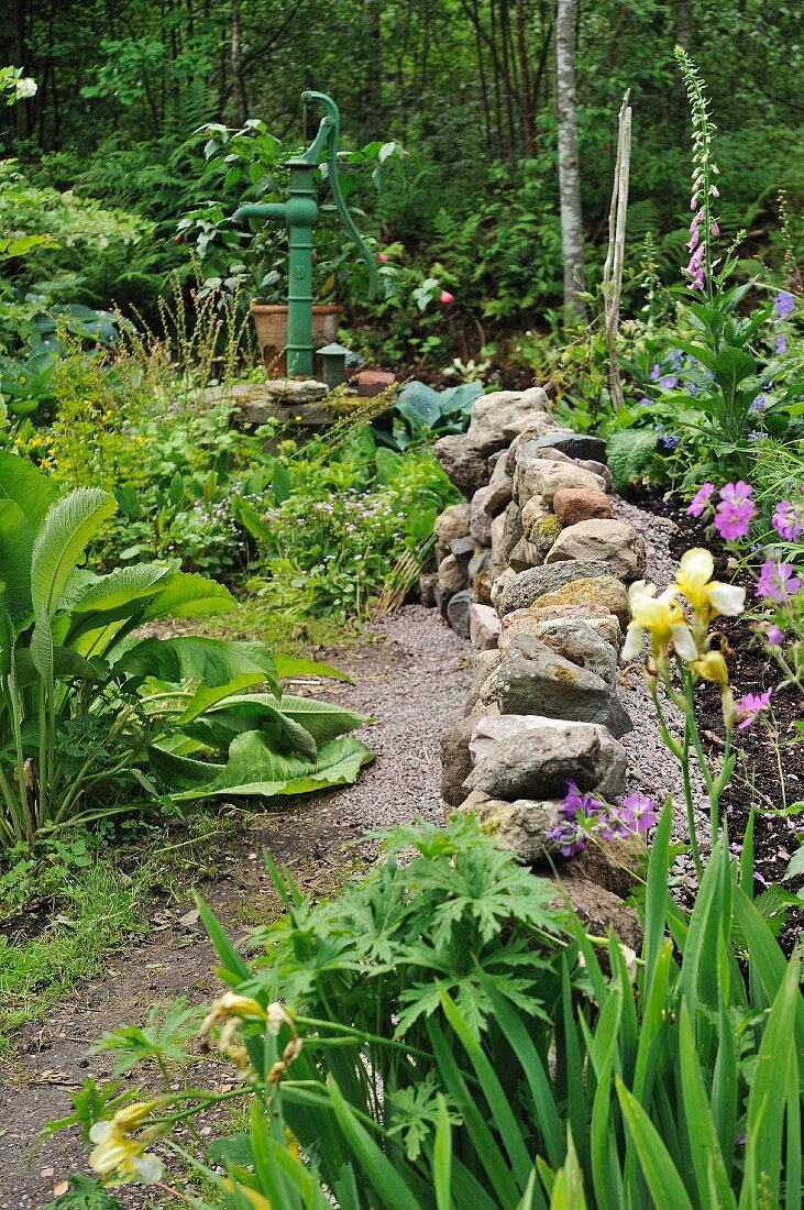 Weg mit Natursteinmauer in dicht bewachsenem Garten